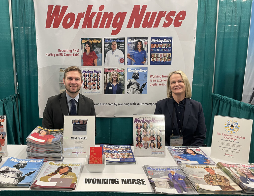 A woman and a man wearing business suits sit at the Working Nurse booth at the ACNL conference.