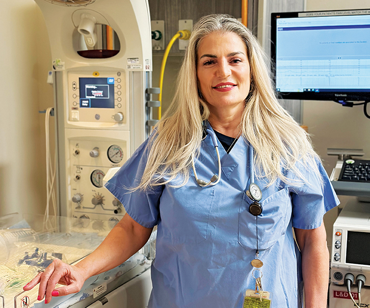 Nurse Gayane Cherechyan in blue scrubs standing in a hospital delivery suite.